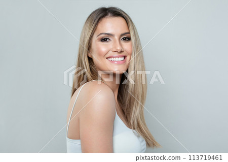 Pretty model woman with fresh clear skin and long healthy blonde hair smiling on white background. F 113719461