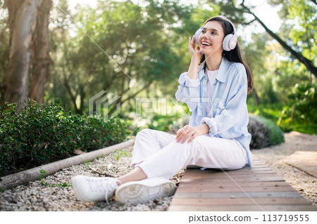 Delighted young woman with white headphones looking up and smiling 113719555