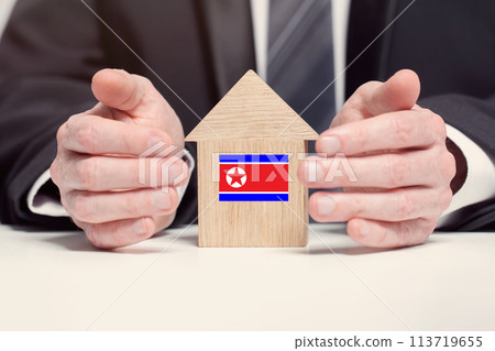 Businessman hand holding wooden home model with North Korean flag. insurance and property concepts 113719655