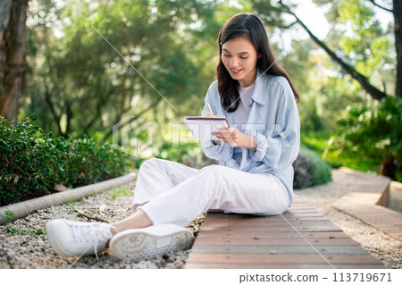 Content woman writing in notebook at public park 113719671