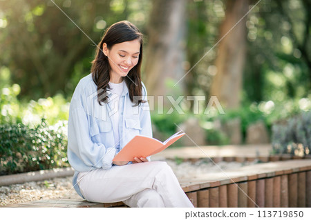 Contemplative young woman enjoying reading a book with an engaging coral cover Contemplative young woman enjoying reading a book with an engaging coral cover 113719850