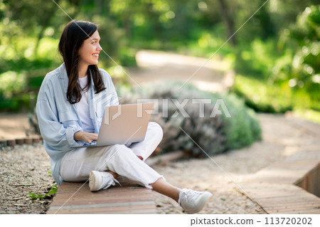 Woman using laptop outdoors at public park 113720202