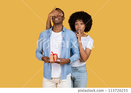Woman surprising man with a gift on yellow Woman surprising man with a gift on yellow 113720255