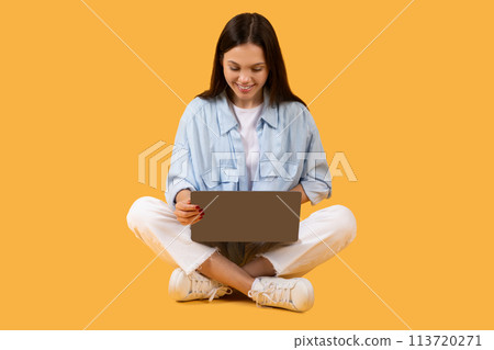 Young lady with laptop sitting cross-legged on yellow background 113720271