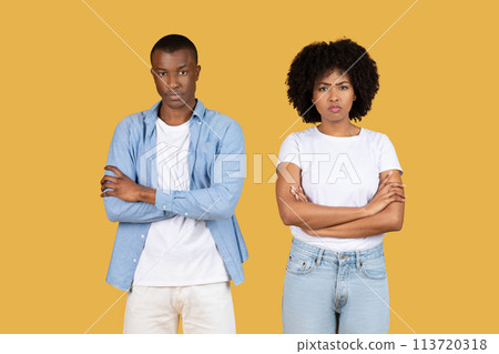 A young African American couple stands facing the camera with serious expressions and arms crossed 113720318