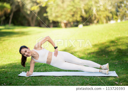 Enthusiastic young woman in a side plank on a yoga mat in the park 113720393