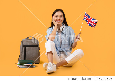 Woman with headphones holding UK flag on yellow background 113720396