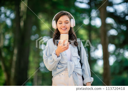 Woman wearing headphones video chatting on smartphone Woman wearing headphones video chatting on smartphone 113720418