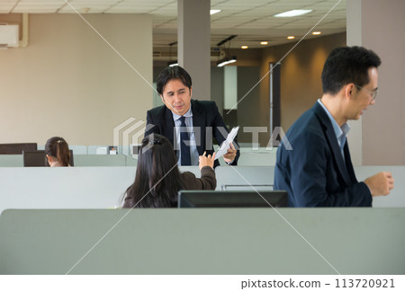 Asian Business man holding paper on hand and working together with woman colleagues in open plan office. Asian Business man holding paper on hand and working together with woman colleagues in open plan office. 113720921