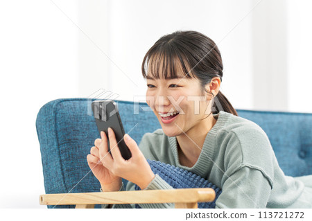 A woman lying on a sofa and looking at her smartphone 113721272