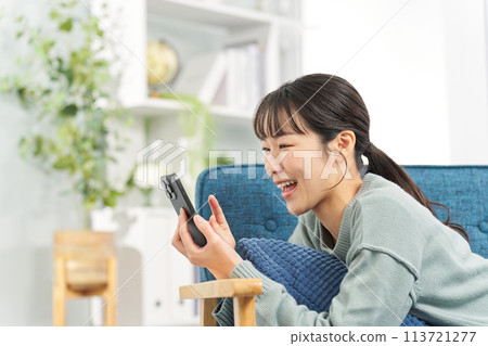 A woman lying on a sofa and looking at her smartphone A woman lying on a sofa and looking at her smartphone 113721277