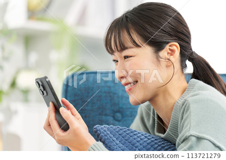 A woman lying on a sofa and looking at her smartphone A woman lying on a sofa and looking at her smartphone 113721279