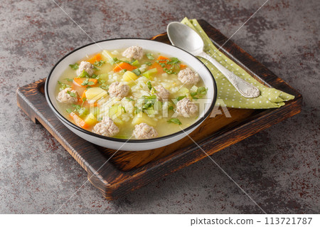Delicious Rice soup with meatballs, celery, carrots, onions, potatoes and herbs close-up in a bowl. Horizontal Delicious Rice soup with meatballs, celery, carrots, onions, potatoes and herbs close-up in a bowl. Horizontal 113721787