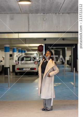 Confident Woman in Chic Winter Coat Standing in Urban Parking Garage Confident Woman in Chic Winter Coat Standing in Urban Parking Garage 113722212
