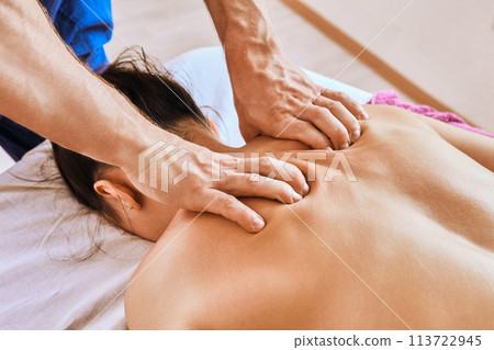 Deep tissue massage therapy for young Caucasian woman lying face down on massage table. 113722945