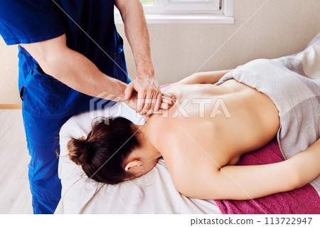Masseur placed one palm on top of other, massaging woman back in shoulder area. Masseur placed one palm on top of other, massaging woman back in shoulder area. 113722947