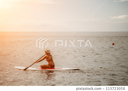 Woman in red bikini on sup board. Happy lady with blond hair in red bathing suit chilling and sunbathing by turquoise sea ocean on sunset. Holiday, vacation and recreational concept. Woman in red bikini on sup board. Happy lady with blond hair in red bathing suit chilling and sunbathing by turquoise sea ocean on sunset. Holiday, vacation and recreational concept. 113723058