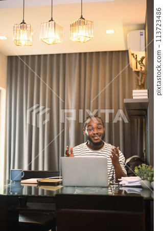 Cheerful African American man having video call on laptop sitting at table in kitchen 113723486