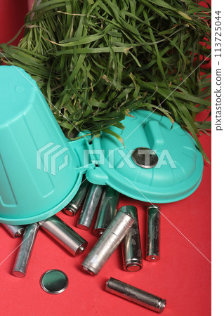 Used finger batteries in a miniature trash can. Fading greens. Pink background. 113725044