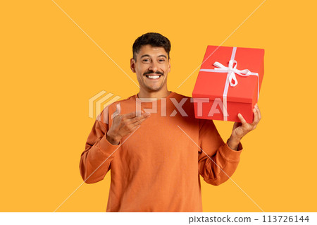 Man cheerfully points to gift box, plain backdrop 113726144