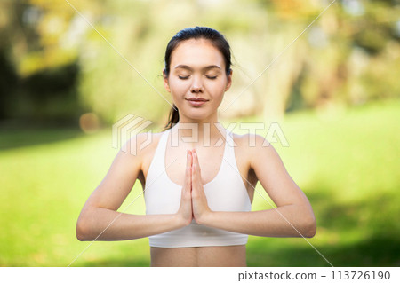Tranquil young woman with eyes closed in Namaste pose, practicing mindful meditation in a bright Tranquil young woman with eyes closed in Namaste pose, practicing mindful meditation in a bright 113726190