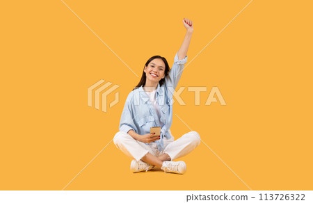 Excited woman making victory gesture on yellow background 113726322