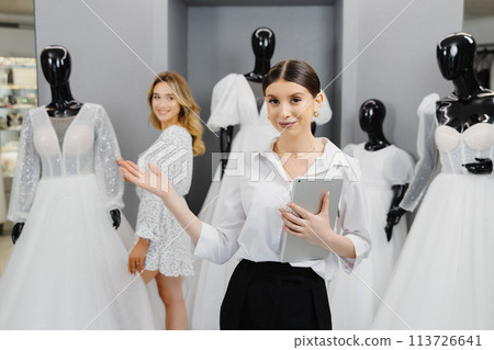Attractive bridal shop owner women use digital tablet help customer choosing wedding gown at the store Attractive bridal shop owner women use digital tablet help customer choosing wedding gown at the store 113726641