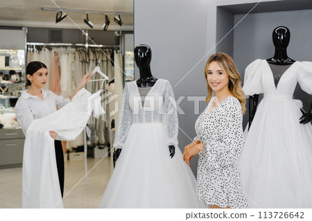Young woman choosing wedding dress in salon. The bride-to-be came to a wedding dress salon to buy a dress 113726642