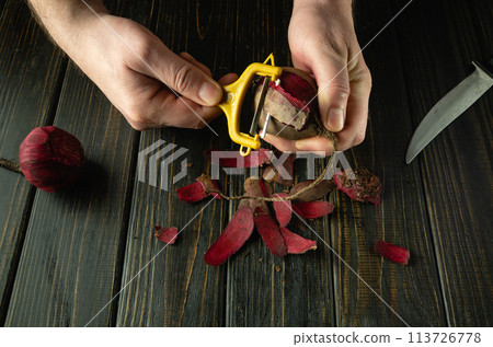 Male hands with a vegetable peeler peel red beets for preparing a vegetable drink or smoothie. Vegetarian food cooking concept 113726778