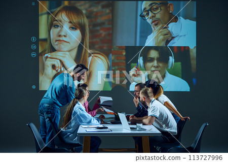 Teammates in office conference room engage in interactive video meeting, using online collaboration tools to discuss tasks and assignments. 113727996