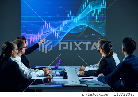 Business professionals sit around conference table in office boardroom, examining digital stock chart displayed on monitor. Business professionals sit around conference table in office boardroom, examining digital stock chart displayed on monitor. 113728083