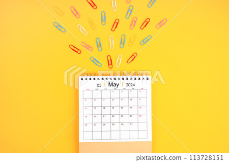 May 2024 desk calendar and colorful metal paperclips on yellow background. 113728151