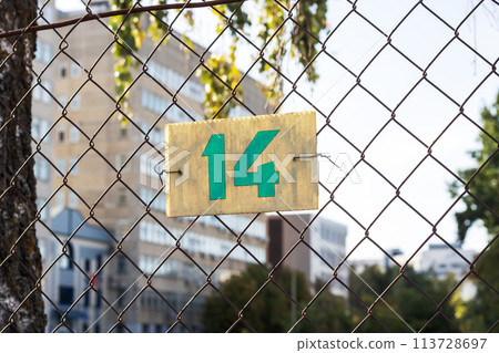 A chainlink fence with the number 14 stands against the sky, made of metal mesh A chainlink fence with the number 14 stands against the sky, made of metal mesh 113728697