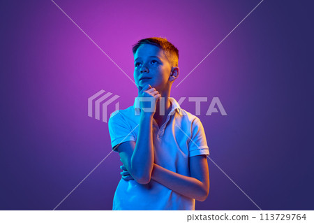 Little boy, school-boy with thoughtful expression looking away in neon light against purple gradient background. 113729764