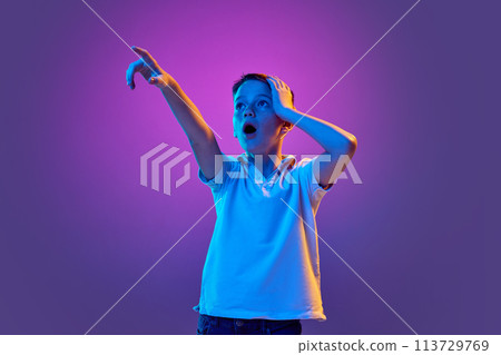 Wow. Surprised boy, in casual attire looking away and pointing to distance in neon light against purple gradient background. Wow. Surprised boy, in casual attire looking away and pointing to distance in neon light against purple gradient background. 113729769