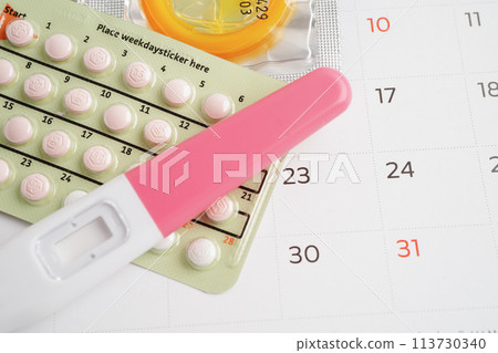 Pregnancy test with birth control pills and condom for female on calendar, ovulation day. Pregnancy test with birth control pills and condom for female on calendar, ovulation day. 113730340