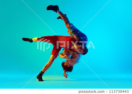 Young men, wrestlers engaged in dynamic and intense competition, grappling for control against blue background in neon light 113730443
