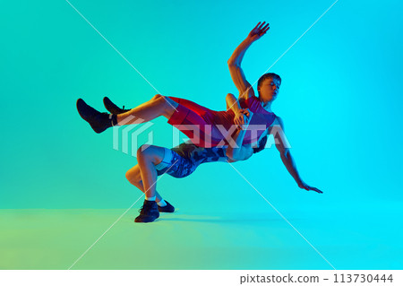 Two men, athletes competing in a wrestling match, demonstrating skills and motivation to win against blue background in neon light 113730444