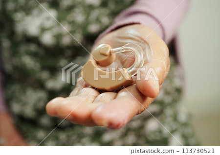 Asian senior woman patient using hearing aid in ear to reduce hearing loss problem. 113730521