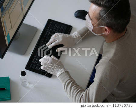 Young woman wearing protective gloves on hands and mask on face working from office or home using laptop on desk. 113730753