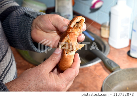 A man tears a bun with filling. 113732078