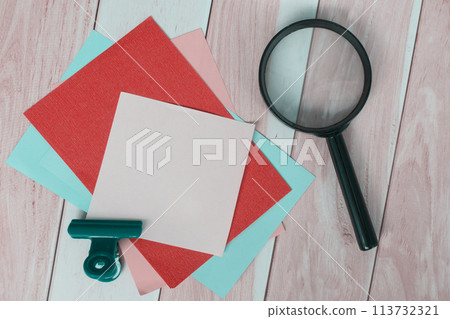 Colorful adhesive paper with magnifying glass on wooden desk. 113732321