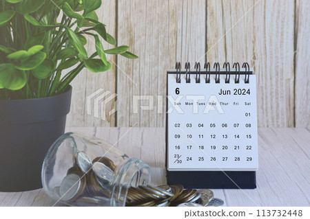 June 2024 desk calendar with stack of coins and potted plant on wooden desk. 113732448
