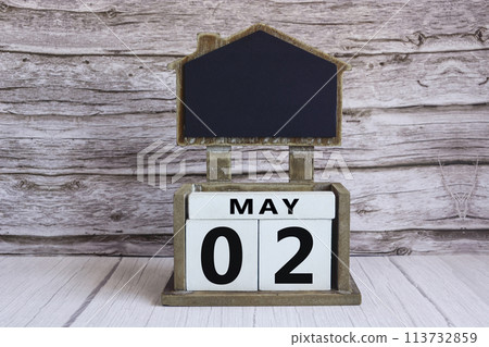 Chalkboard with May 02 date on white cube block on wooden table. 113732859