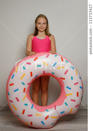 Beautiful child girl with pink rubber inflatable ring swimming pool float standing on white studio 113733427