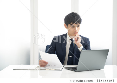 Male businessman working on a laptop and checking documents Male businessman working on a laptop and checking documents 113733461