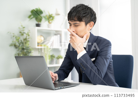 Male businessman yawning while working on a laptop Male businessman yawning while working on a laptop 113733495