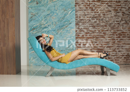 Glamorous young woman make-up and long hair wearing yellow dress posing sitting 113733852