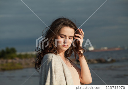 Glamorous young woman model with brown hair and natural make-up walking along the shore of resort 113733970
