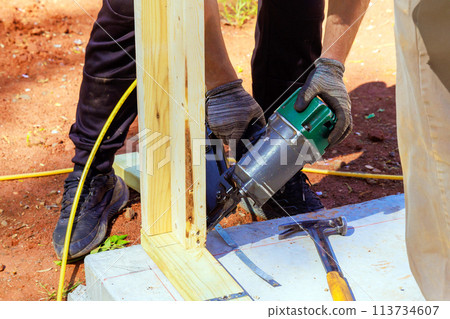 Framer uses an air nail hammer to install beams in wooden frame Framer uses an air nail hammer to install beams in wooden frame 113734607